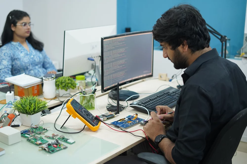Two engineers testing a board with a multimeter at their desk